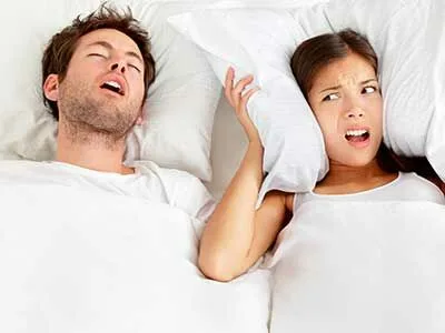A man snoring while his partner covers her ears with a pillow
