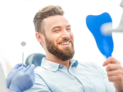 A patient laughing in the dental chair while holding a mirror